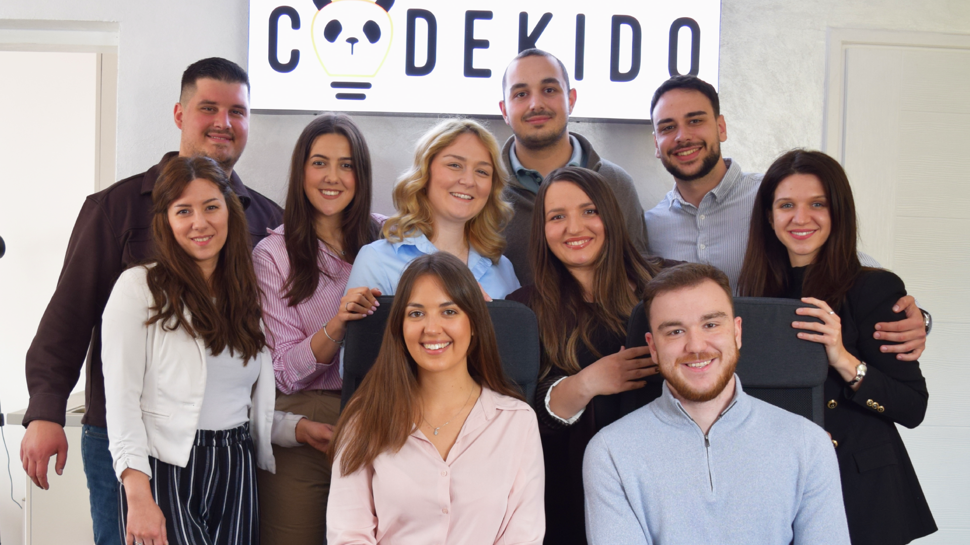 Codekido tim zajedno u kancelariji ispred CODEKIDO znaka